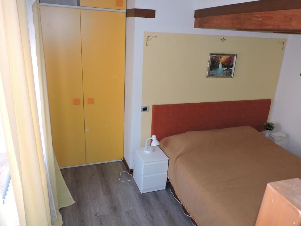 A bedroom with a bed, a nightstand, a wardrobe, and a small table with a lamp.