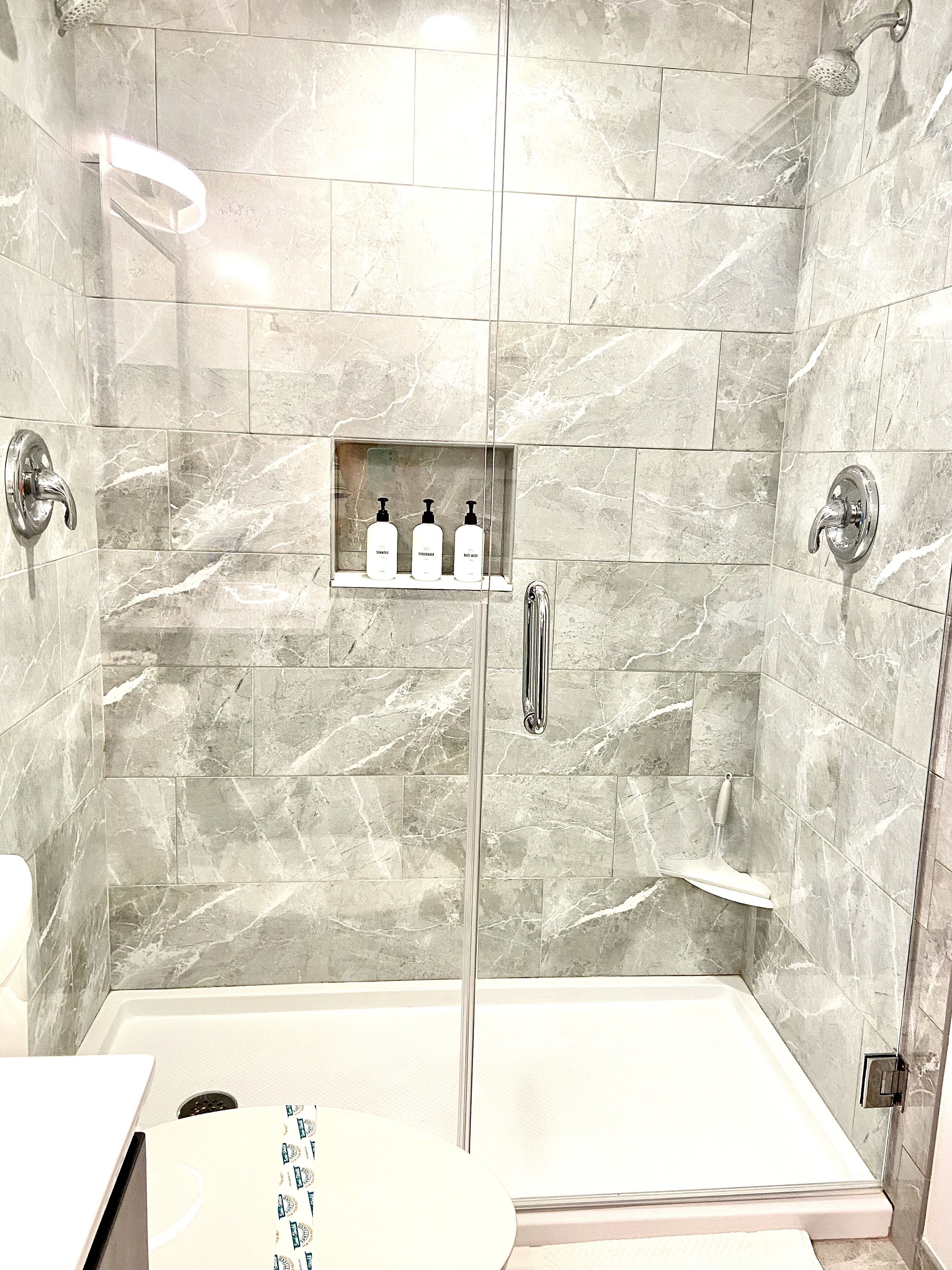 Ein modernes Badezimmer mit einer Duschkabine, einer integrierten Ablage für Toilettenartikel und einer Badewanne.