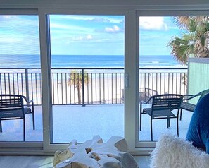 A room with a sliding glass door leading to a balcony with a view of the beach and ocean. There are two chairs on the balcony. - Organic Beach Retreat (Daytona Beach Shores)