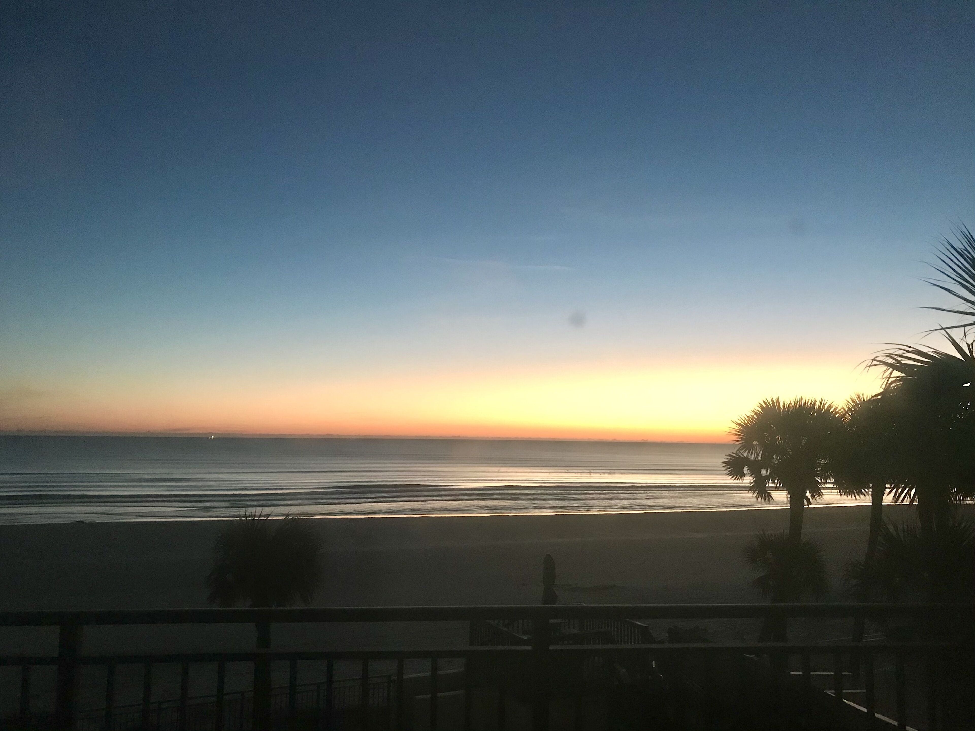Blick auf einen Strand bei Sonnenuntergang, mit blauem Himmel und ruhiger See.