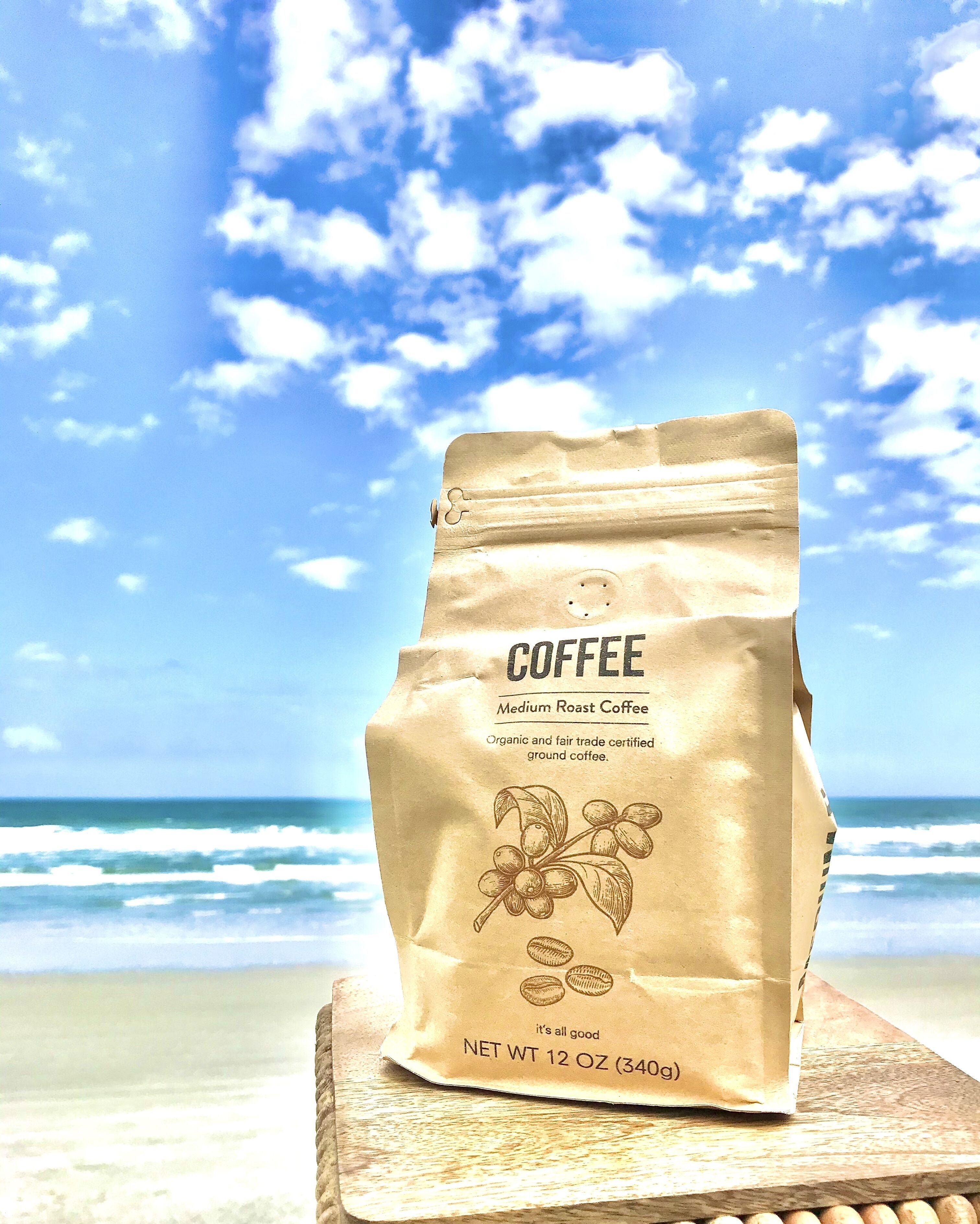 Um saco de café sobre uma superfície de madeira, com uma praia e oceano ao fundo.