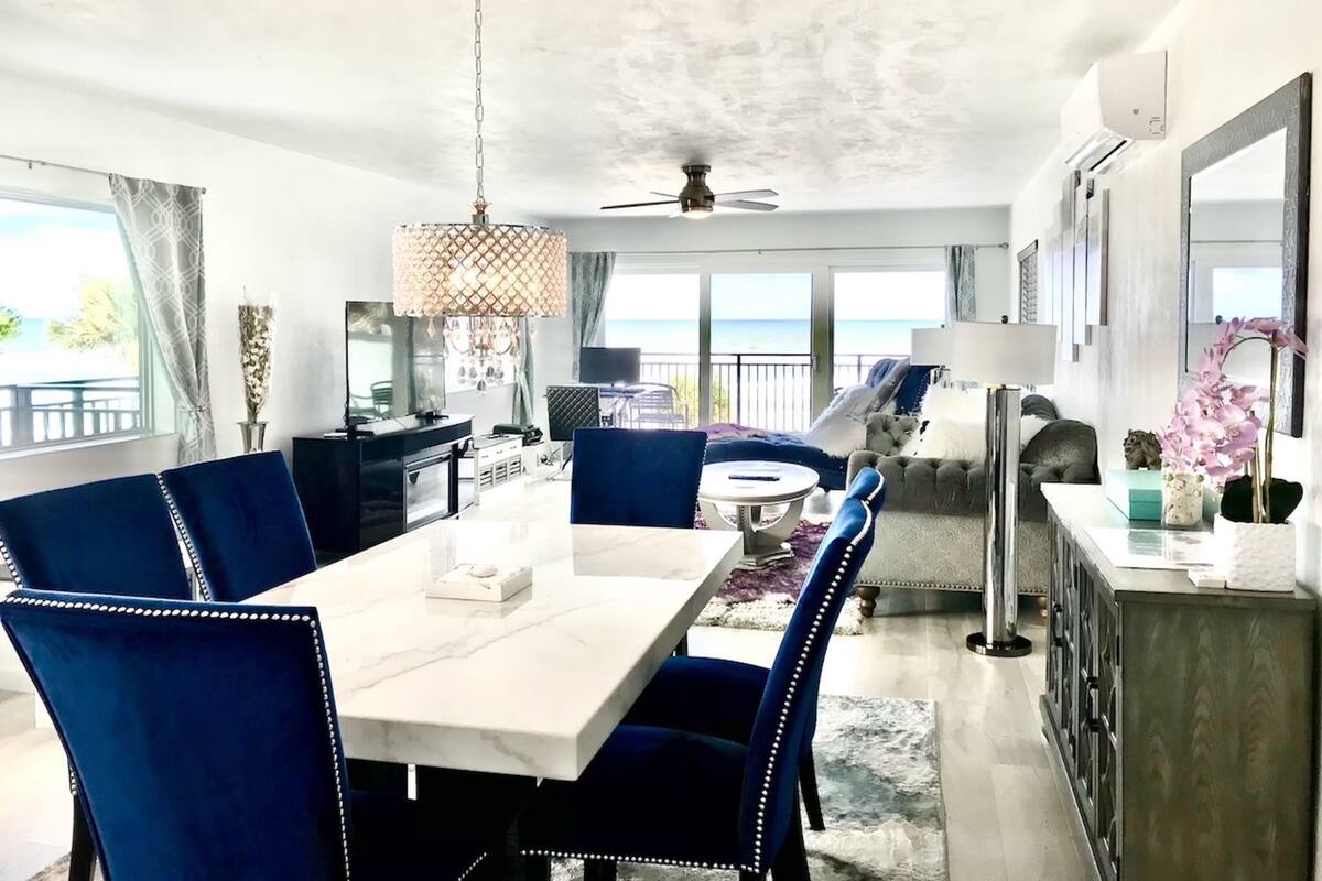 A modern dining area with a white table, blue upholstered chairs, and a chandelier.