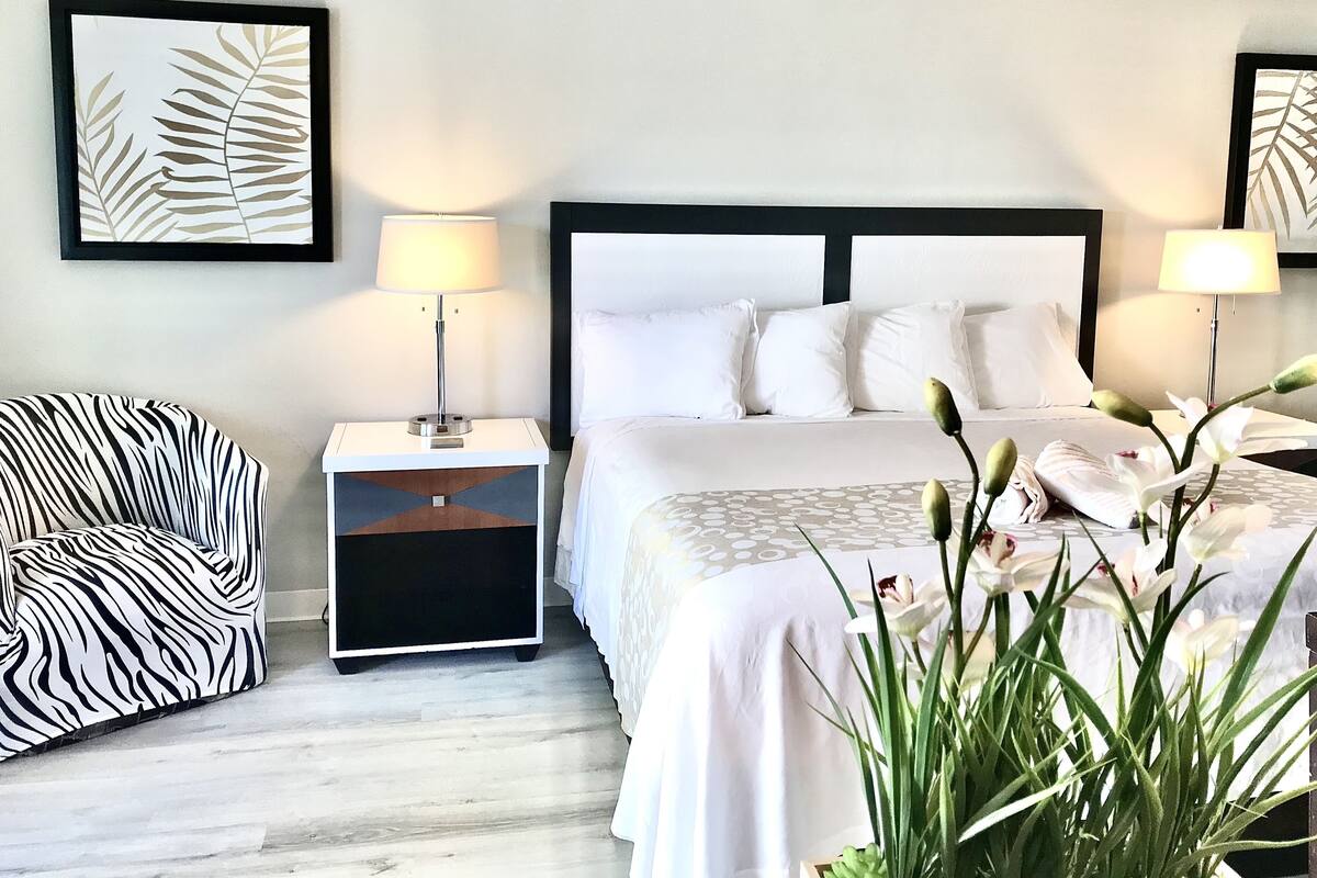 A hotel room with a bed, two nightstands, a zebra-patterned chair, and a ceiling fan.
