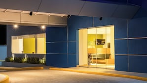 A modern building with a glass entrance, a visible sign with text, and a well-lit interior. - One Puebla Serdan (Puebla)