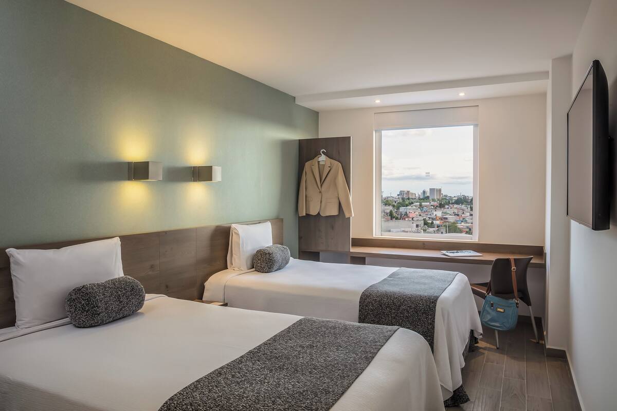A hotel room with two beds, a city view, a coat rack, and a desk with a chair.