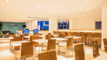 A modern dining area with wooden chairs and tables, a reception desk, and a blue wall with signage.