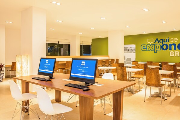 A modern conference room with two computer stations, white chairs, and a green wall with a sign. - One Puebla Serdan (Puebla)