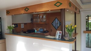 A reception desk with a computer, a phone, and a glass vase with flowers. There are shelves with books and a mirror above the desk. - H41 Inn Freiburg (Gundelfingen)