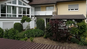 A two-story house with a balcony, large windows, and a garden with various plants. - H41 Inn Freiburg (Gundelfingen)