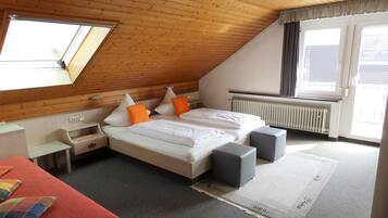 A bedroom with a sloped ceiling, a large window, a bed with pillows, a bedside table, and a radiator.