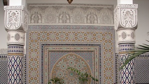 Una habitación con detalles de azulejos intrincados, una fuente central y una cama con cabecera blanca.
