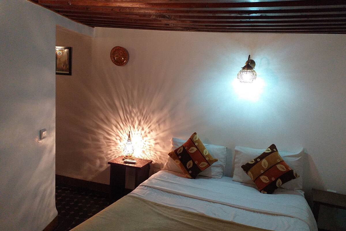 Una camera da letto con un letto, due comodini, una sveglia a parete e un punto luce a parete.