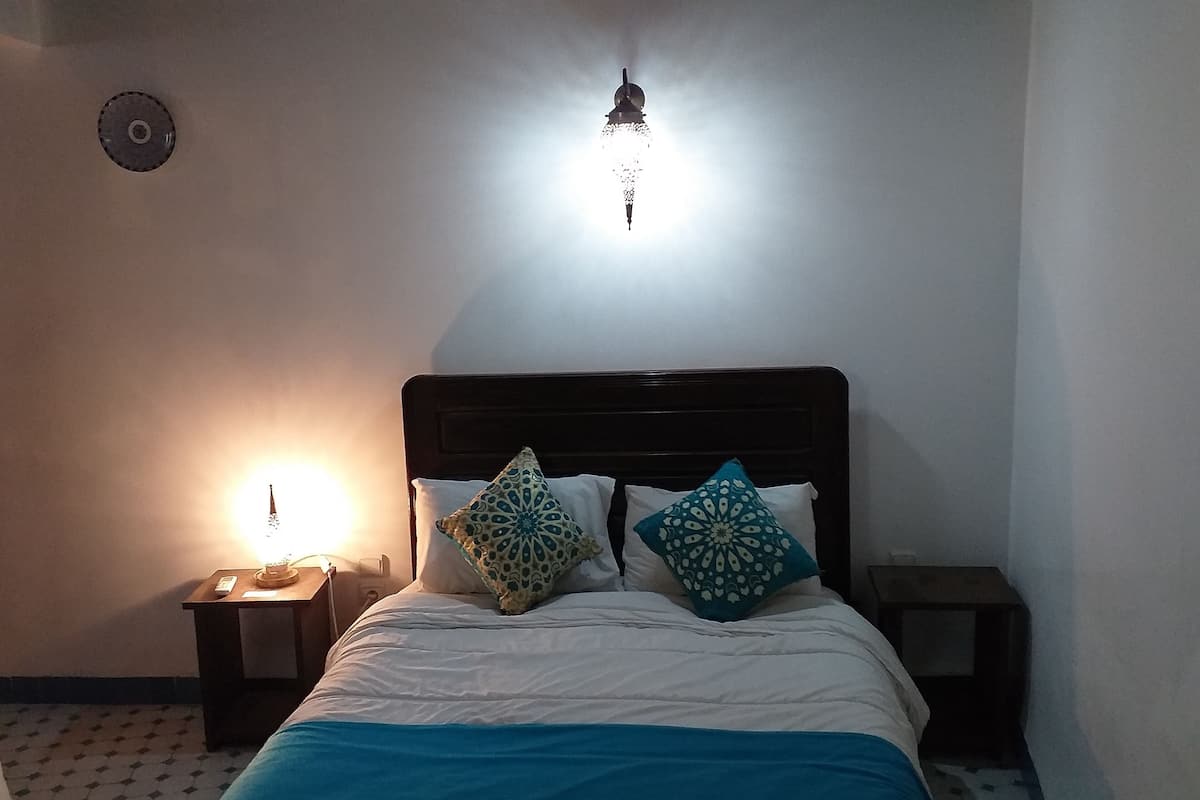 Una camera da letto con un letto, due comodini, una sveglia a muro e una lampada a sospensione.