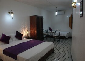 Quarto de hotel com cama, uma pequena mesa com cadeira, armário e duas luzes fixadas na parede.