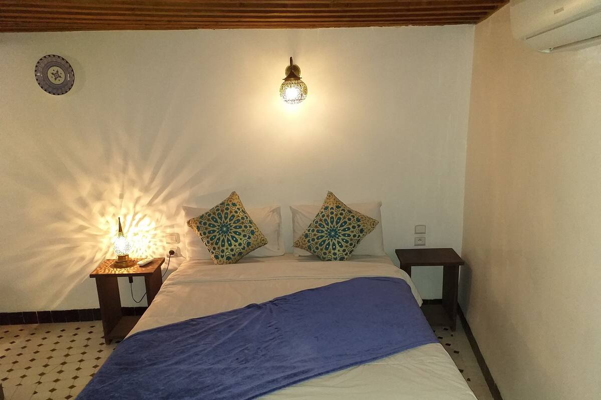 Una camera da letto con un letto, un comodino, una lampada a parete e cuscini decorati.