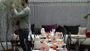 Montaje de un bufé de desayuno con diversos platos, como croissants, fruta y bebidas, sobre una mesa con mantel rojo.