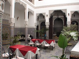 Interior com mesas e cadeiras, paredes estampadas e colunas decorativas.