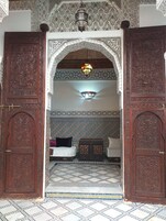Uma porta ornamentada com esculturas detalhadas, parede de azulejos estampados e um candeeiro suspenso.