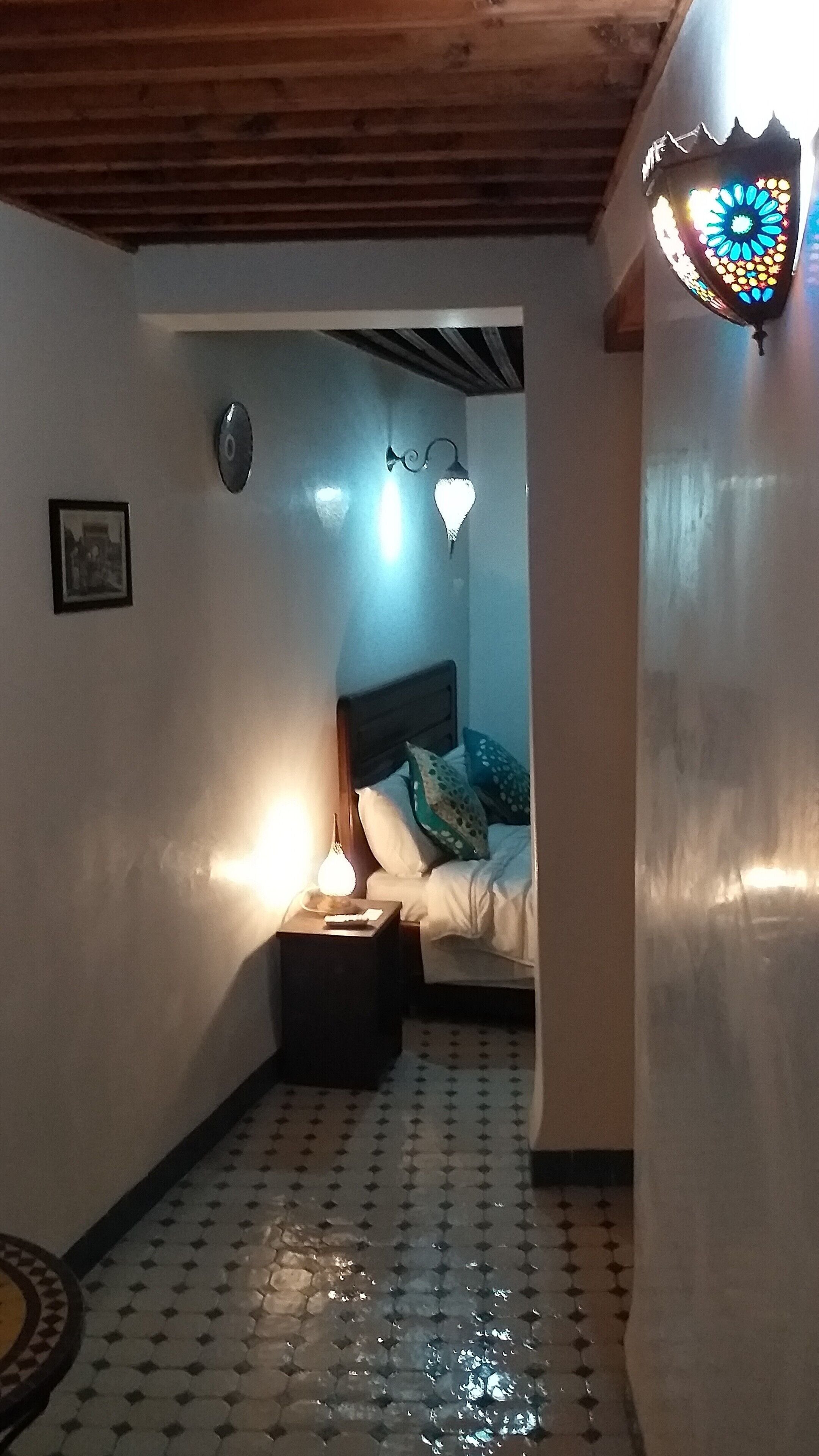 Una habitación pequeña y acogedora con una cama, una mesita de noche, un reloj de pared y una lámpara decorativa.