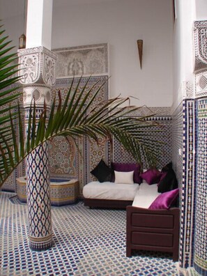 A room with a patterned floor, a bed with pillows, a decorative vase, and intricate wall designs. - Riad Sheryne - Fes (Fes)