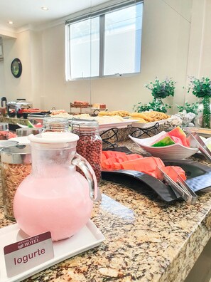 A buffet with various food items and a pitcher of pink beverage labeled 'logurte'. - Avenida Palace Hotel (Joinville)