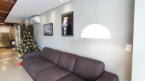 A modern living room with a grey sofa, a Christmas tree, and a wall-mounted air conditioner. - Avenida Palace Hotel (Joinville)