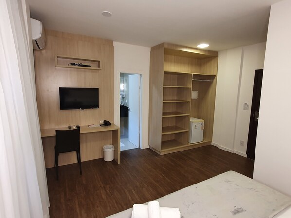 Une chambre d’hôtel équipée d’un bureau en bois, d’une télévision, d’une armoire et d’un petit réfrigérateur.