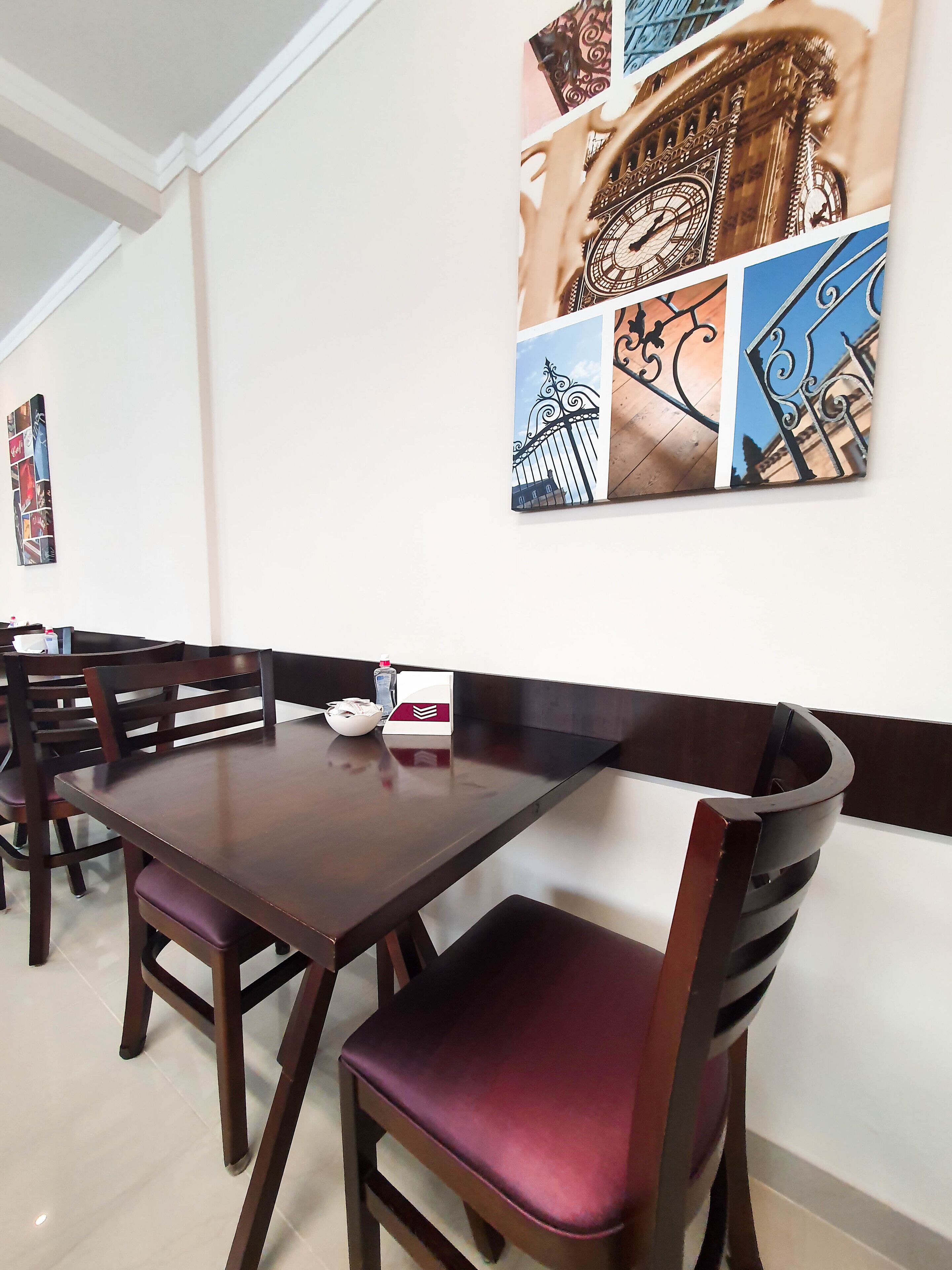 A dining area with a long table and chairs, a wall-mounted artwork depicting architectural elements, and a whiteboard with a red and white logo.