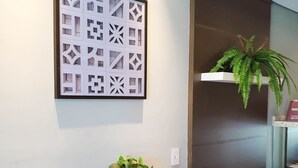 A reception desk with a patterned wall art, a potted plant, and a book display. - Avenida Palace Hotel (Joinville)