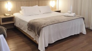A hotel room with a large bed, wooden headboard, bedside lamps, a nightstand, and a window with curtains. - Avenida Palace Hotel (Joinville)