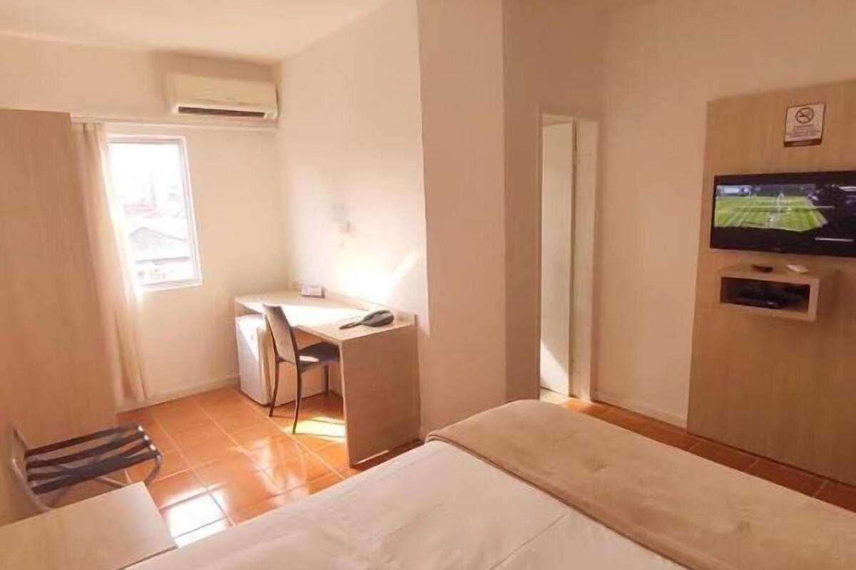 Una habitación de hotel con una cama, un escritorio, una silla, un televisor y una ventana.
