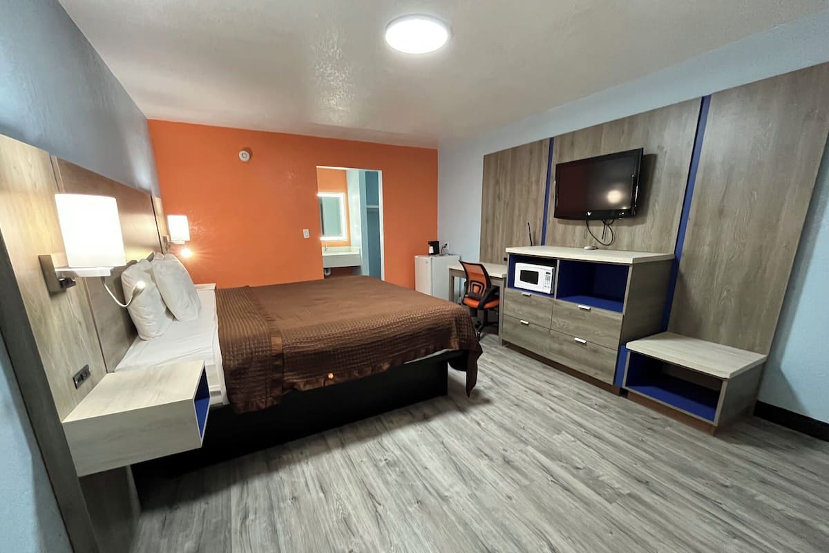 A modern hotel room with a bed, a desk, a microwave, and a TV.