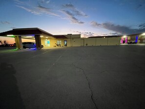 A parking garage with a car under a covered area, a building with a flat roof, and a clear sky.