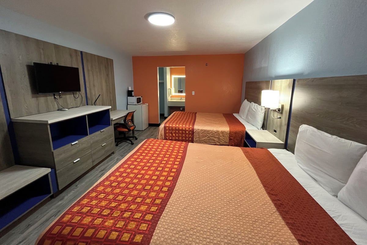 A hotel room with two beds, a desk, a TV, and a microwave.