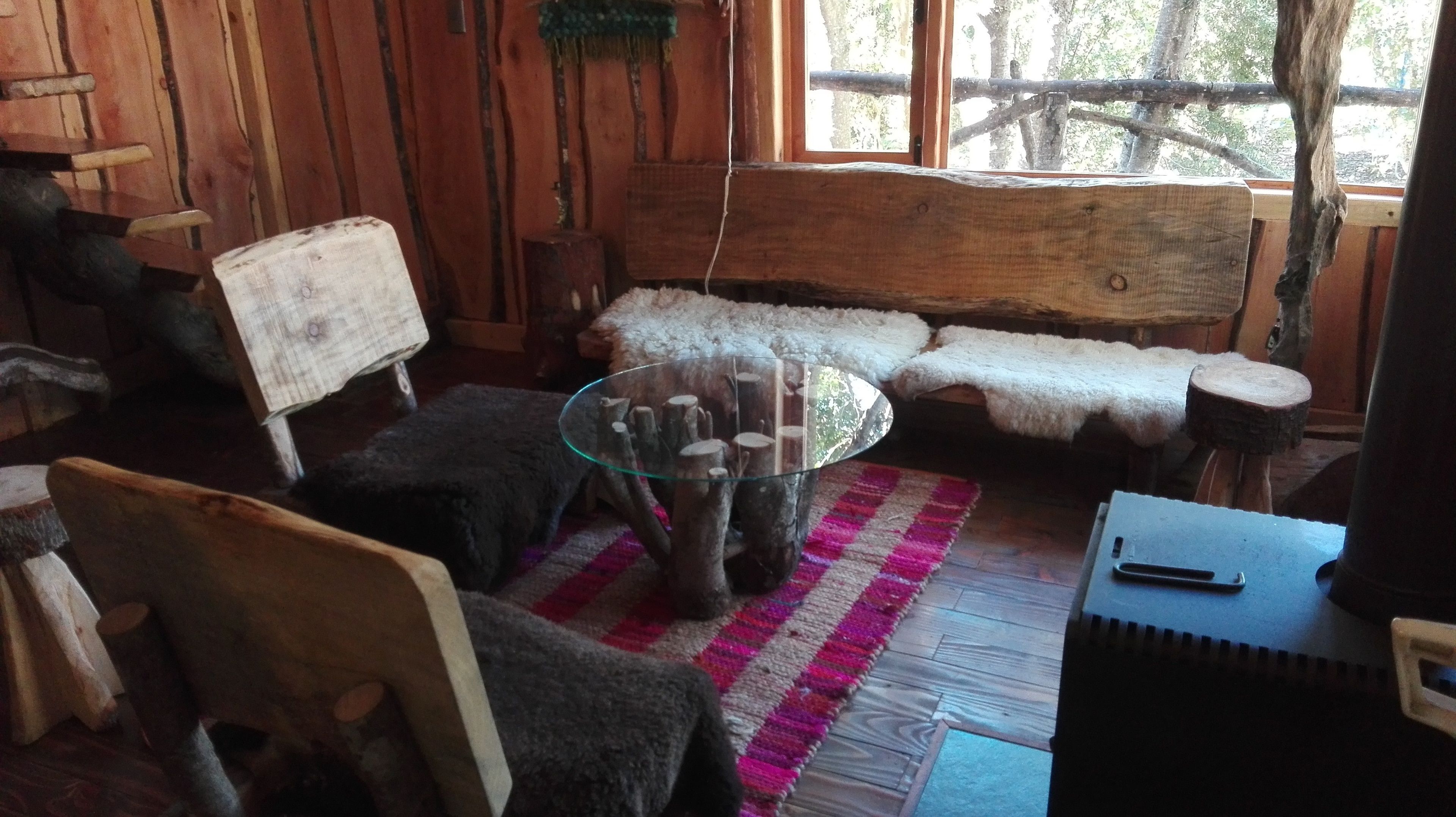 A rustic wooden interior with a glass coffee table surrounded by wooden furniture, including a bench and chairs.