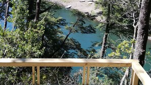 A wooden deck overlooking a river with boats, surrounded by dense forest. - Cabañas Rústicas Pucón (Pucón)