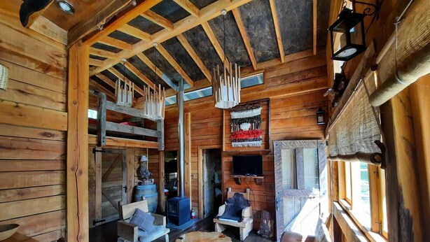 A rustic cabin interior with wooden walls, a stone fireplace, and a cozy seating area. - Cabañas Rústicas Pucón (Pucón)