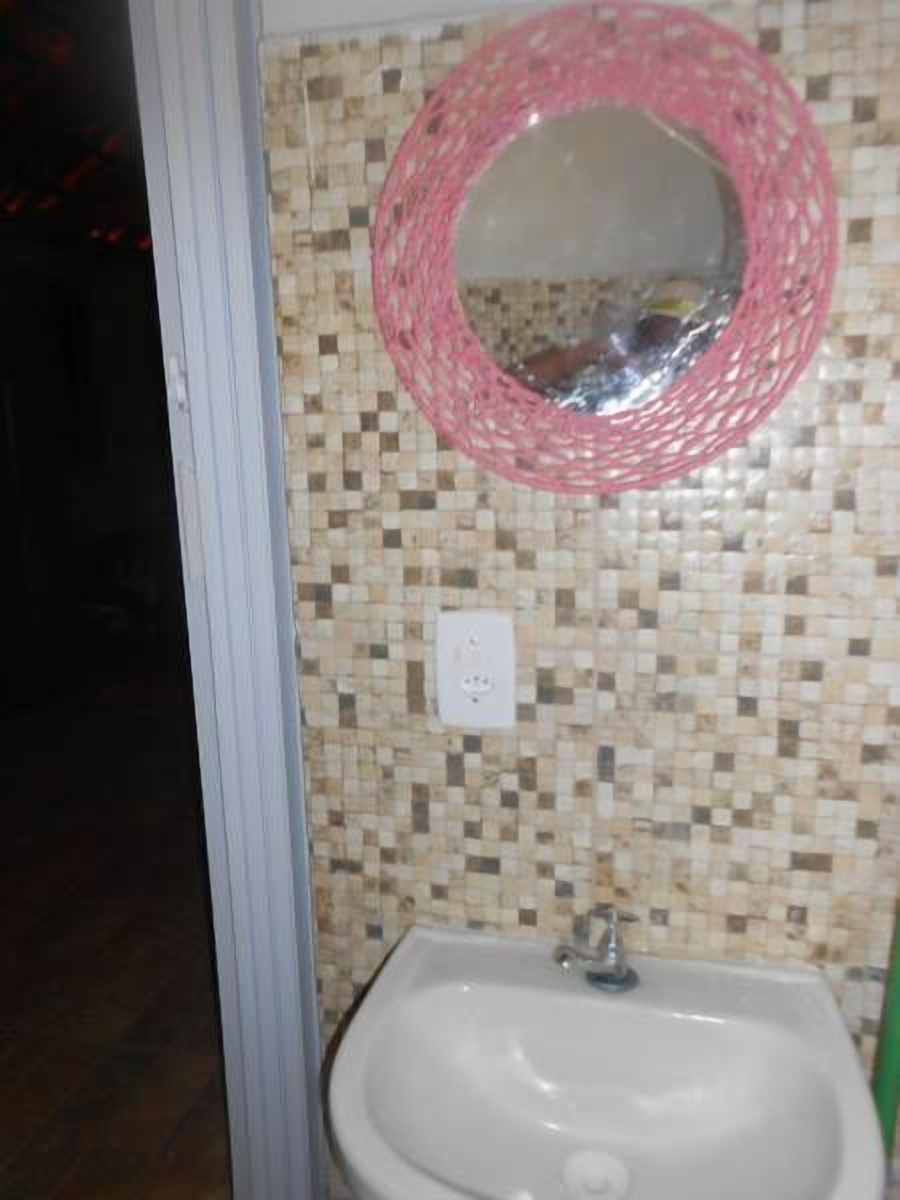 A bathroom with a mosaic tile backsplash, a white sink, and a pink woven mirror.
