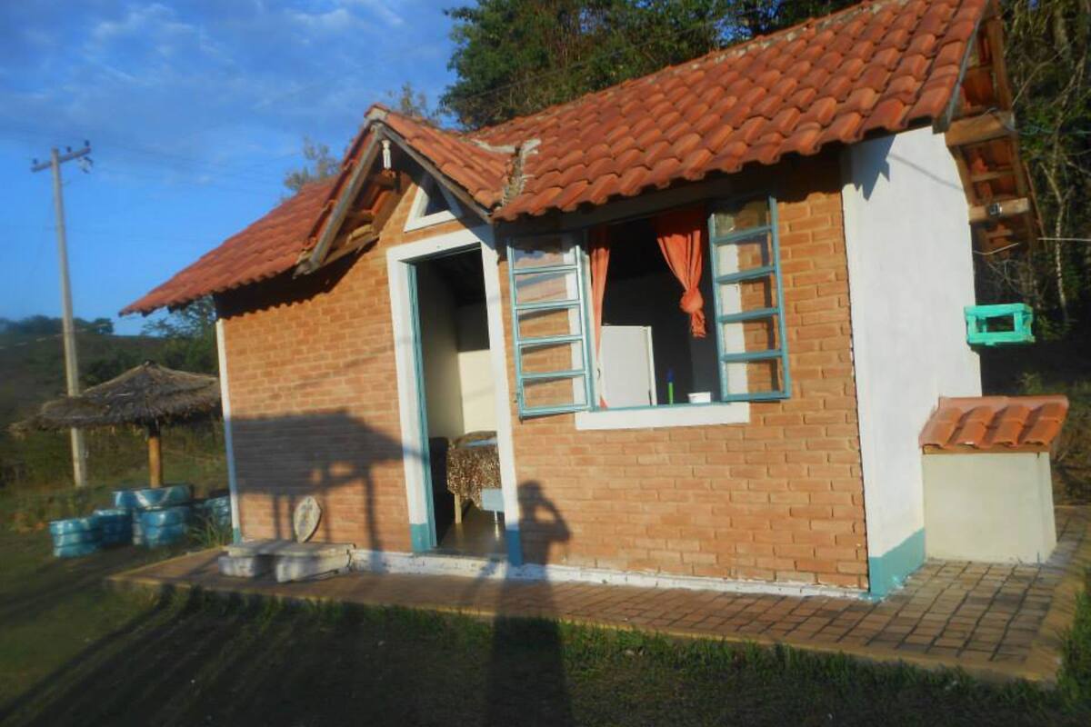 A small brick house with a red-tiled roof, a single door, and a window with curtains.