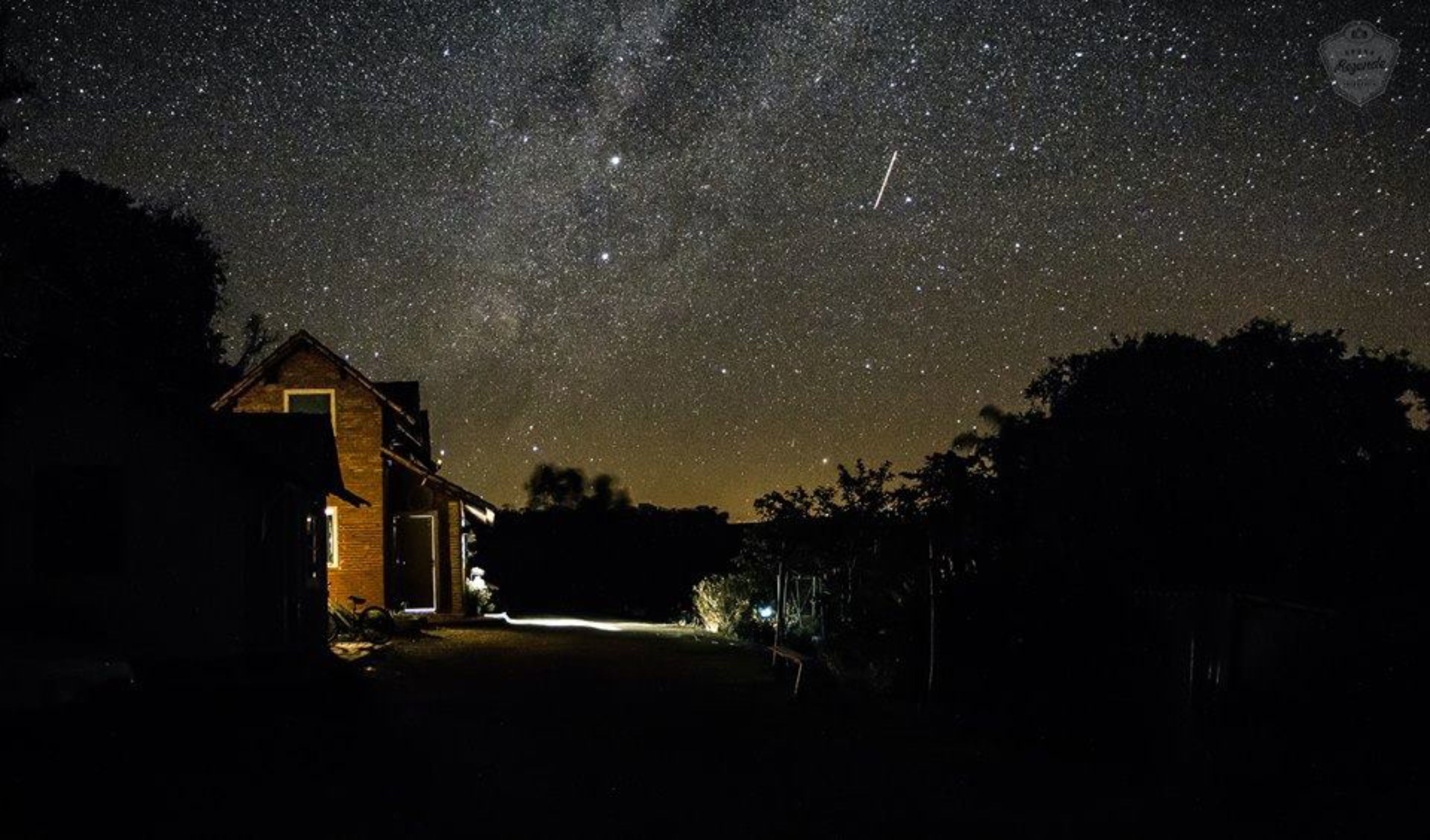 A house with a lit interior, under a starry night sky.