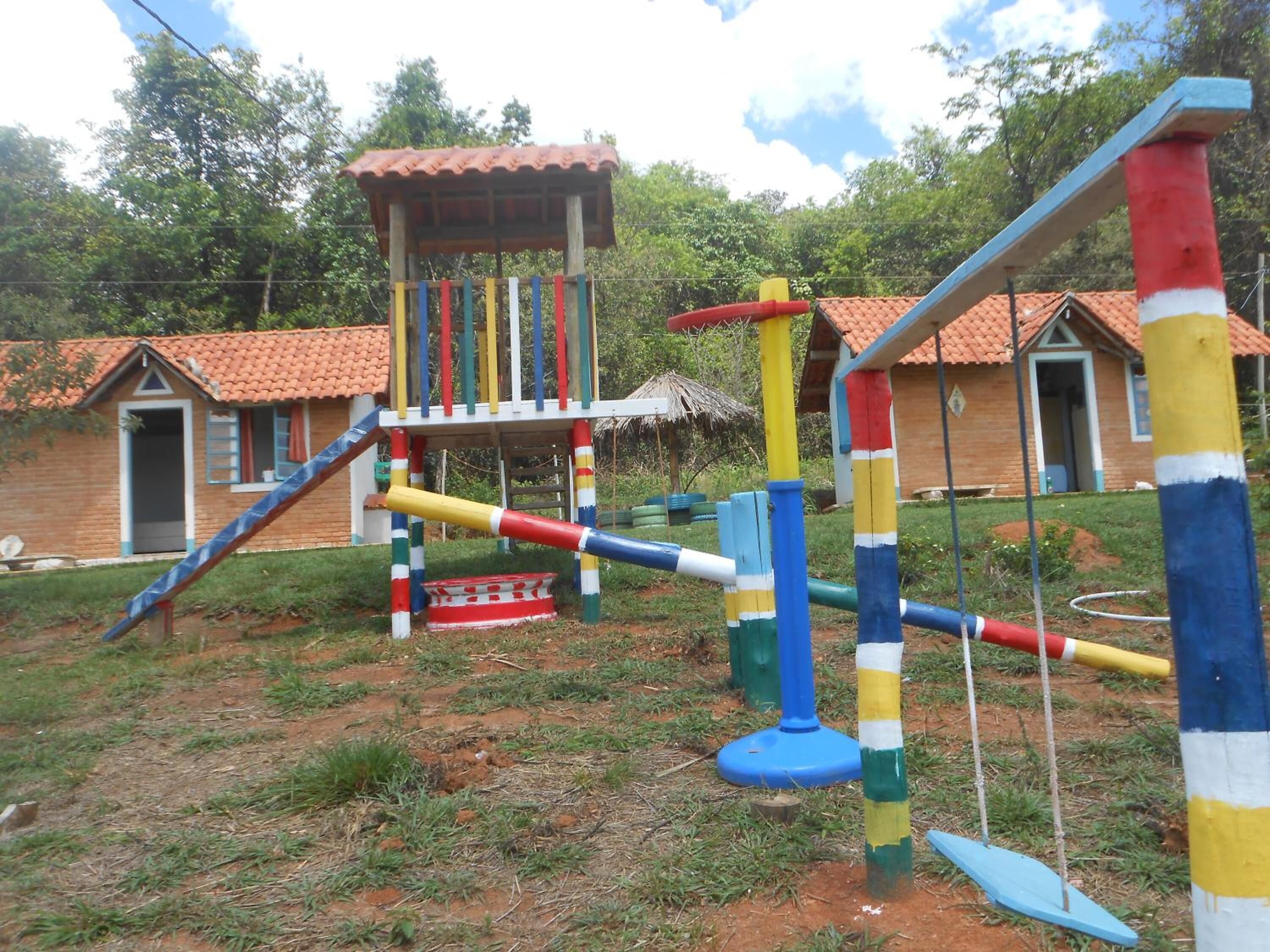 A playground with colorful play structures, a small hut, and a house with a red-tiled roof in the background.