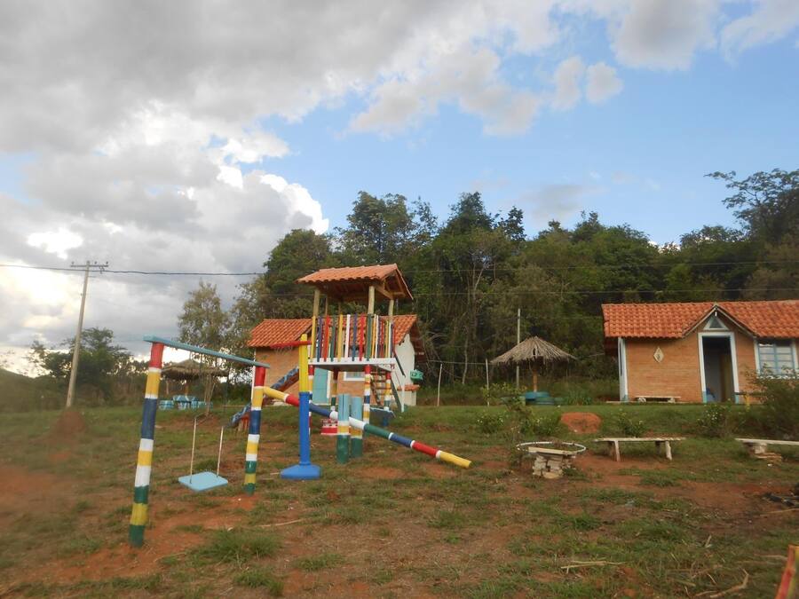 Un parque infantil con juegos de colores y una casita de techo rojo en un entorno rural.