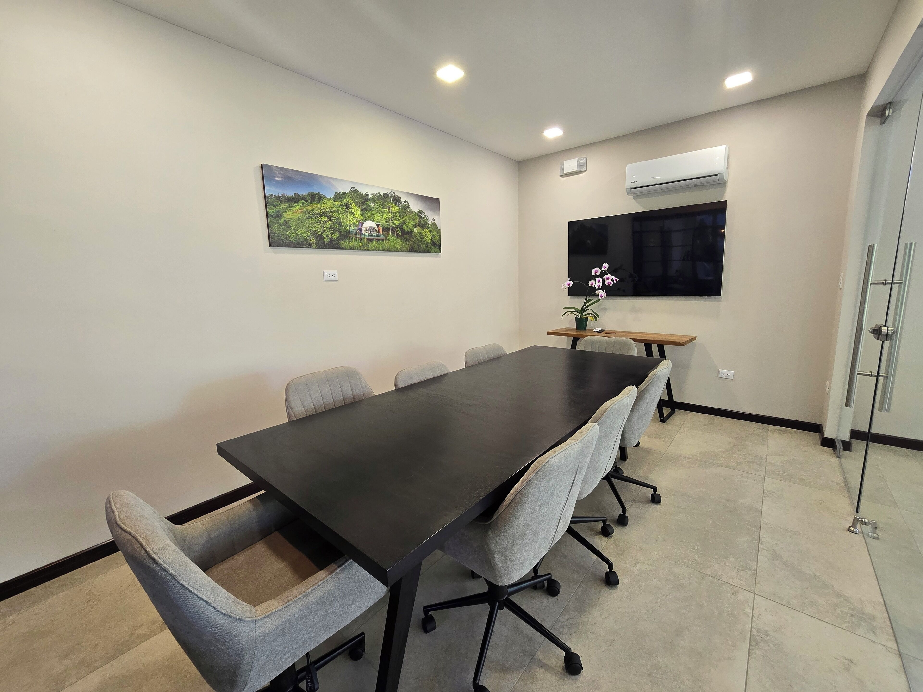 Un salón de conferencias con una larga mesa, seis sillas, una planta en maceta y un cuadro en la pared.