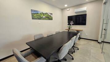 Un salón de conferencias con una larga mesa, seis sillas, una planta en maceta y un cuadro en la pared.