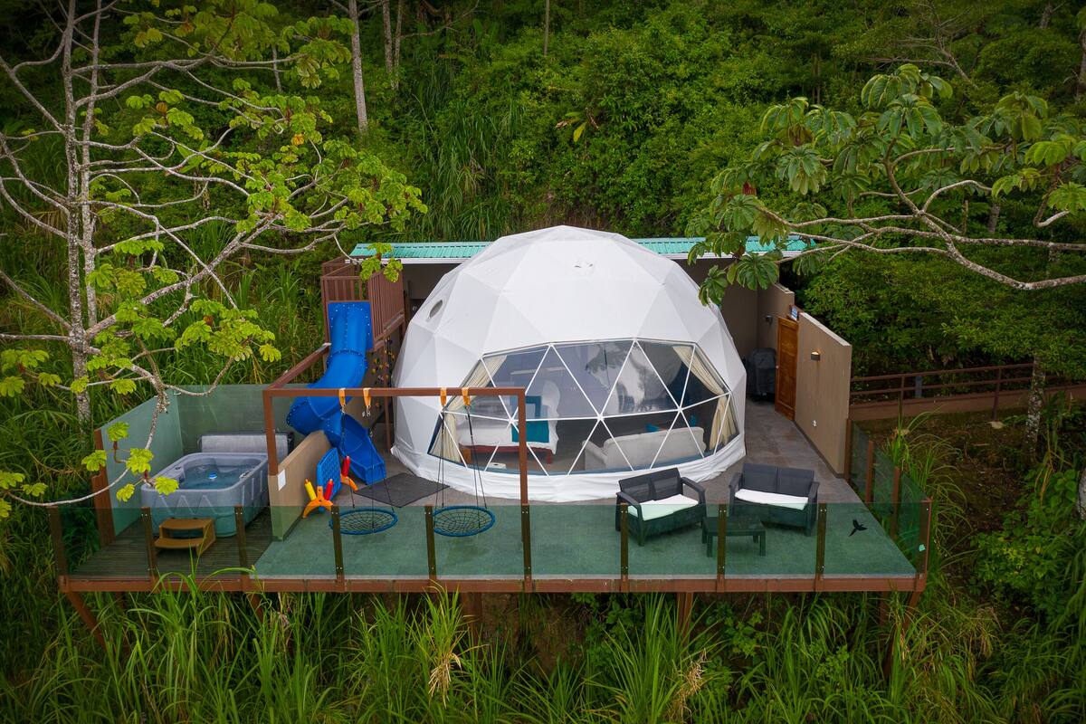 A geodesic dome structure with a glass floor, surrounded by lush greenery.