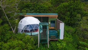 A geodesic dome structure surrounded by dense greenery, with a small wooden building adjacent to it. - Chira Glamping Resort Monteverde (Monteverde)