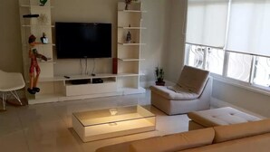 A modern living room with a flat-screen TV, a sofa, a coffee table, and a chair. - Etours - Luminoso 3 Quartos Copacabana Souza Lima (Rio de Janeiro)