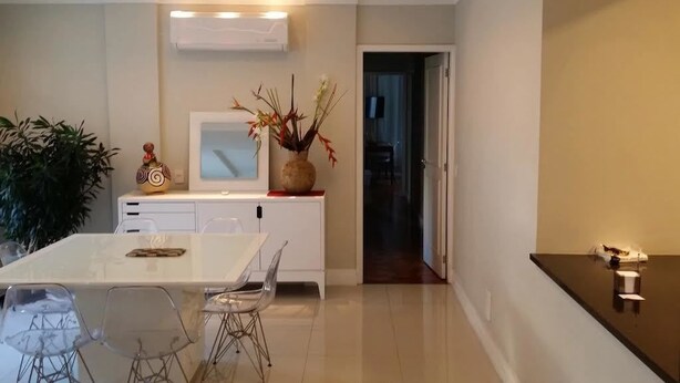 A modern kitchen with a white countertop, a dining table with chairs, and a decorative vase with plants. - Etours - Luminoso 3 Quartos Copacabana Souza Lima (Rio de Janeiro)