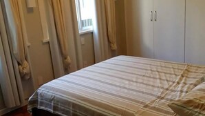A bedroom with a bed, curtains, a window, and a wardrobe. - Etours - Luminoso 3 Quartos Copacabana Souza Lima (Rio de Janeiro)