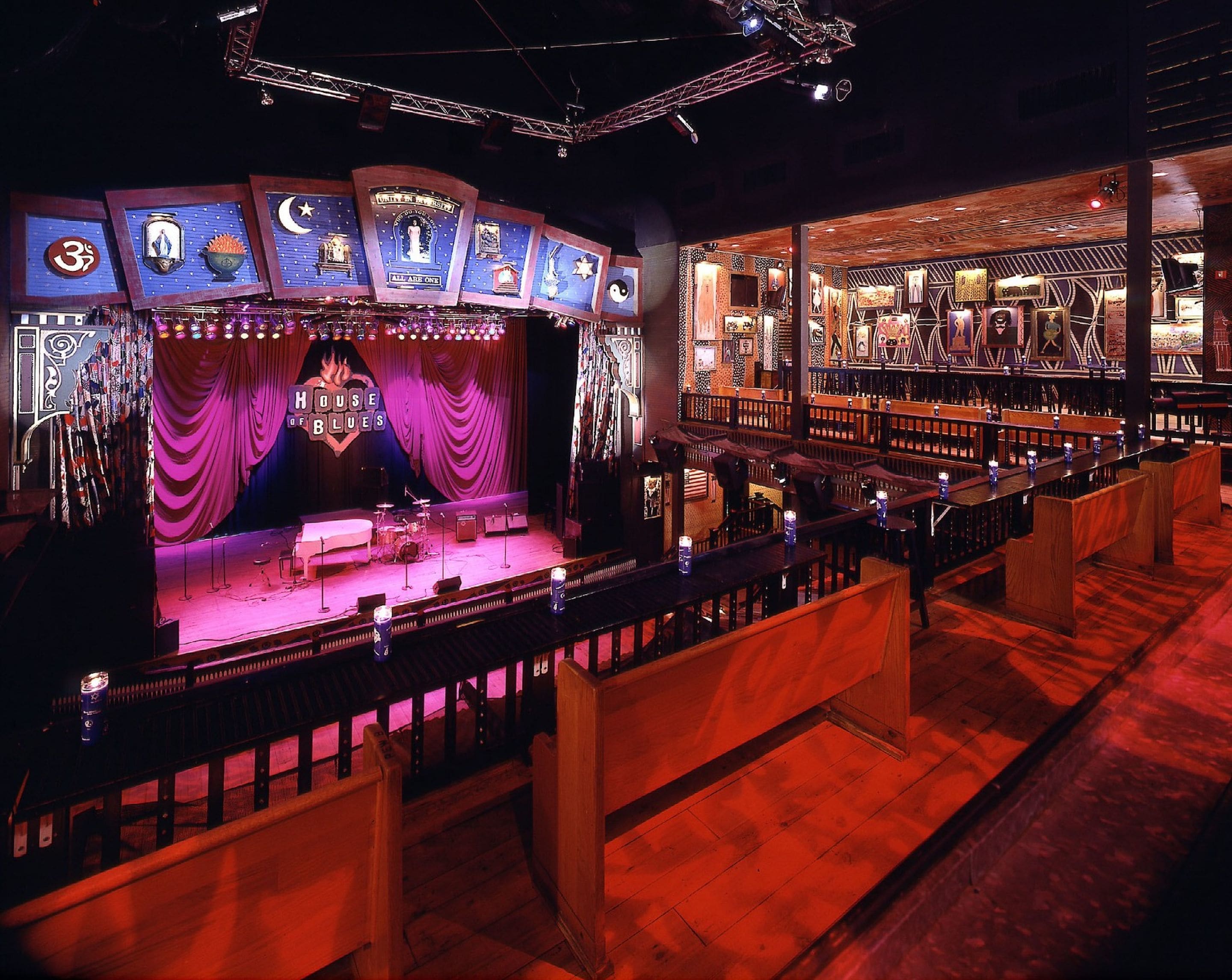 Une scène sur laquelle est affiché un panneau indiquant « House of Blues », ainsi qu’un espace bar avec des sièges en bois et un mur orné de motifs.